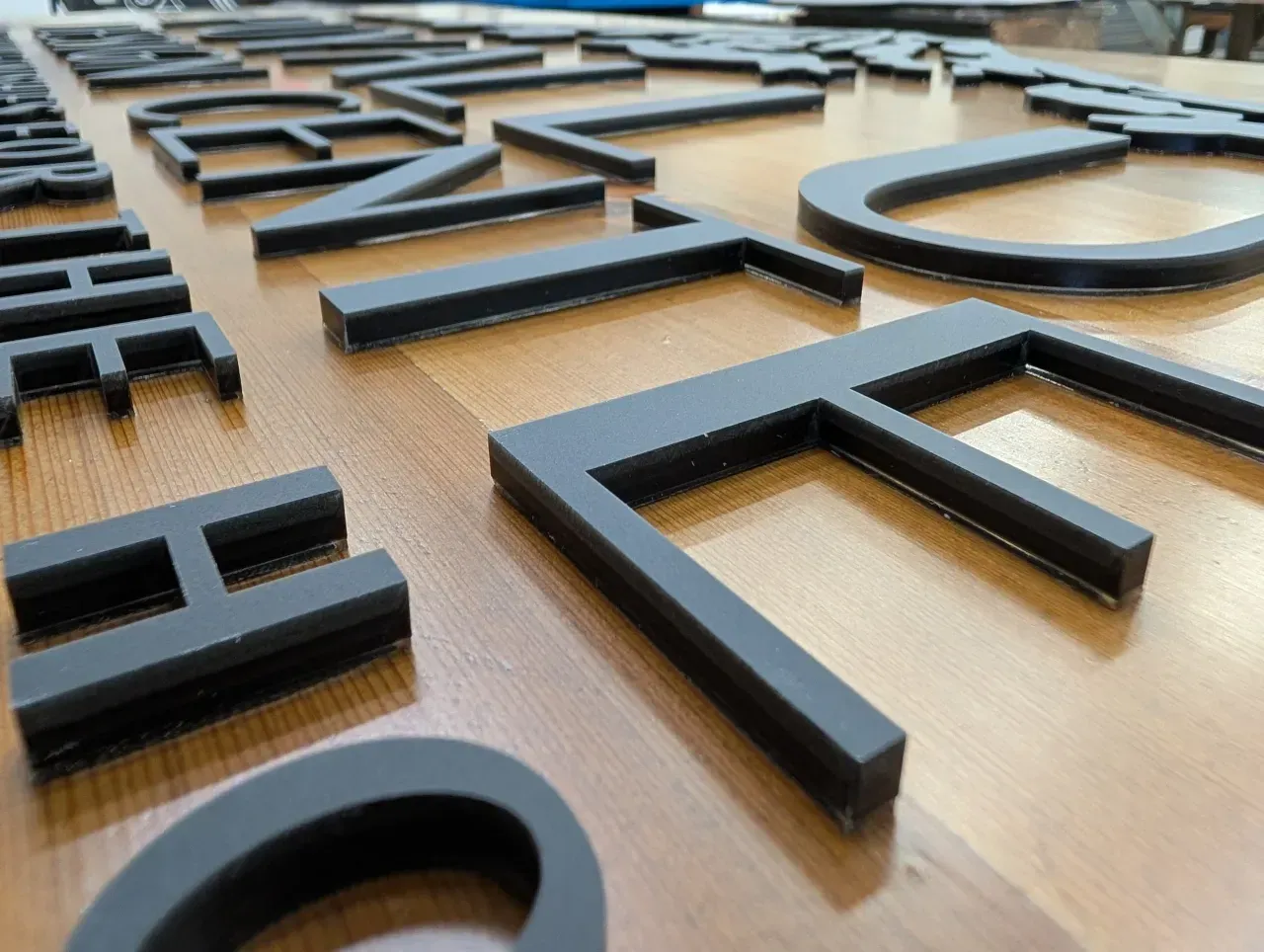 Close-up of raised black letters on a light wooden surface, viewed at an angle.