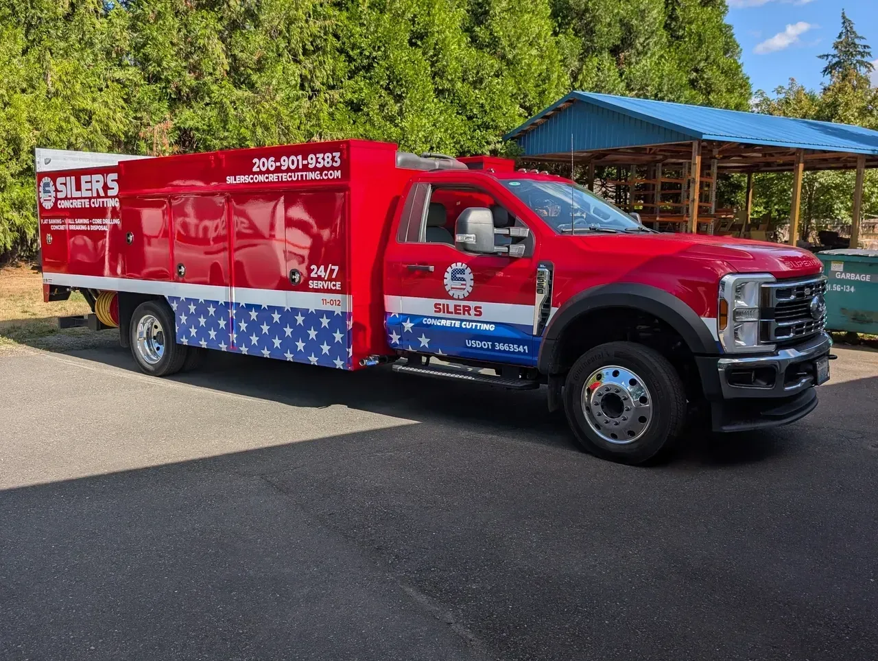 Red and silver service truck parked on a driveway beside a blue-roofed building.
