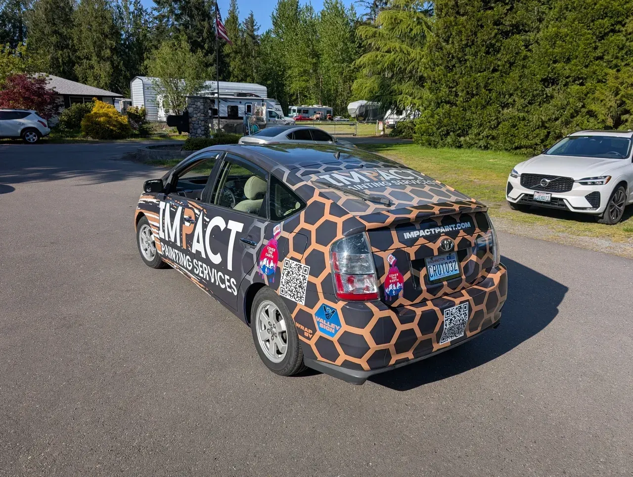 Camouflaged compact car parked on a suburban street with houses and trees in the background.