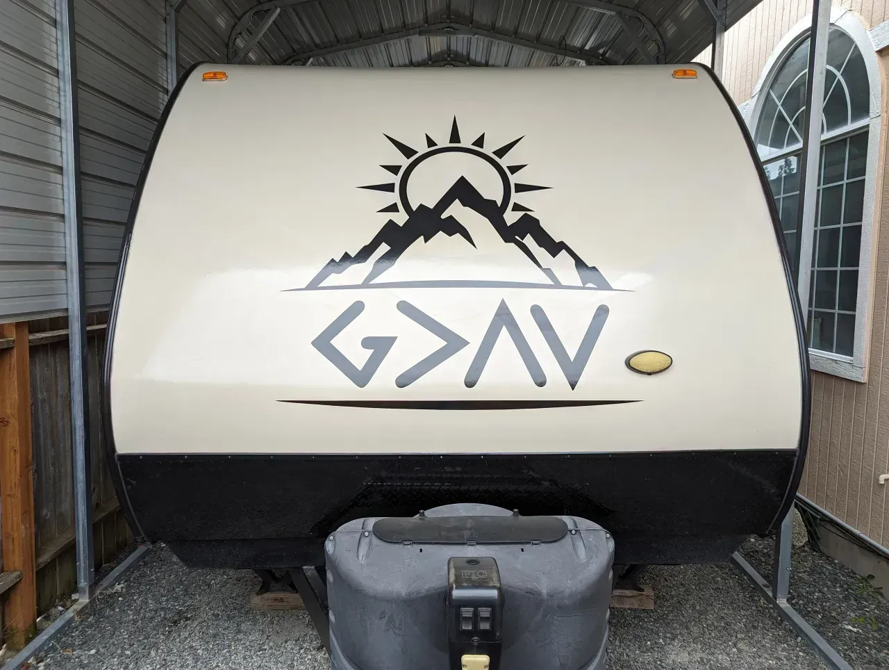 White camper trailer with mountain logo and “G>AV” decal in a covered storage area