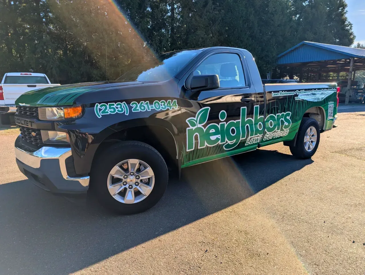 Black pickup truck with green “neighbors” graphics parked outdoors in sunlight