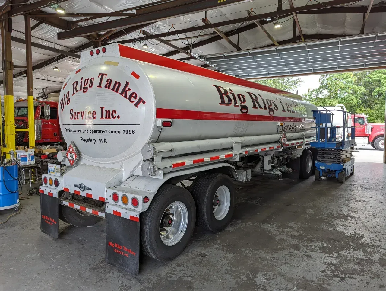 Big tanker service truck parked in an industrial garage with a blue forklift nearby