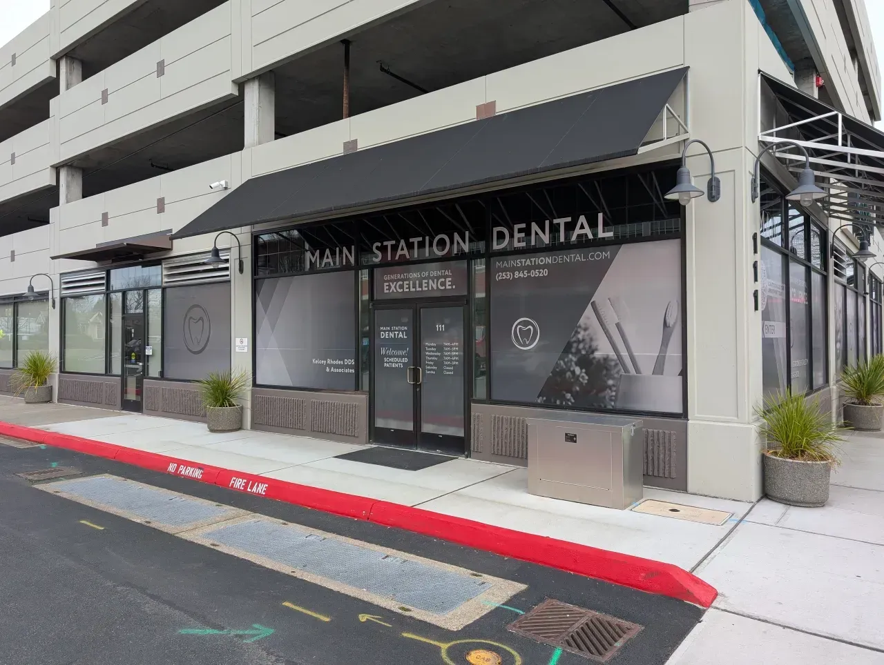 Exterior of a dental clinic with black awning, glass doors, and potted plants by the curb