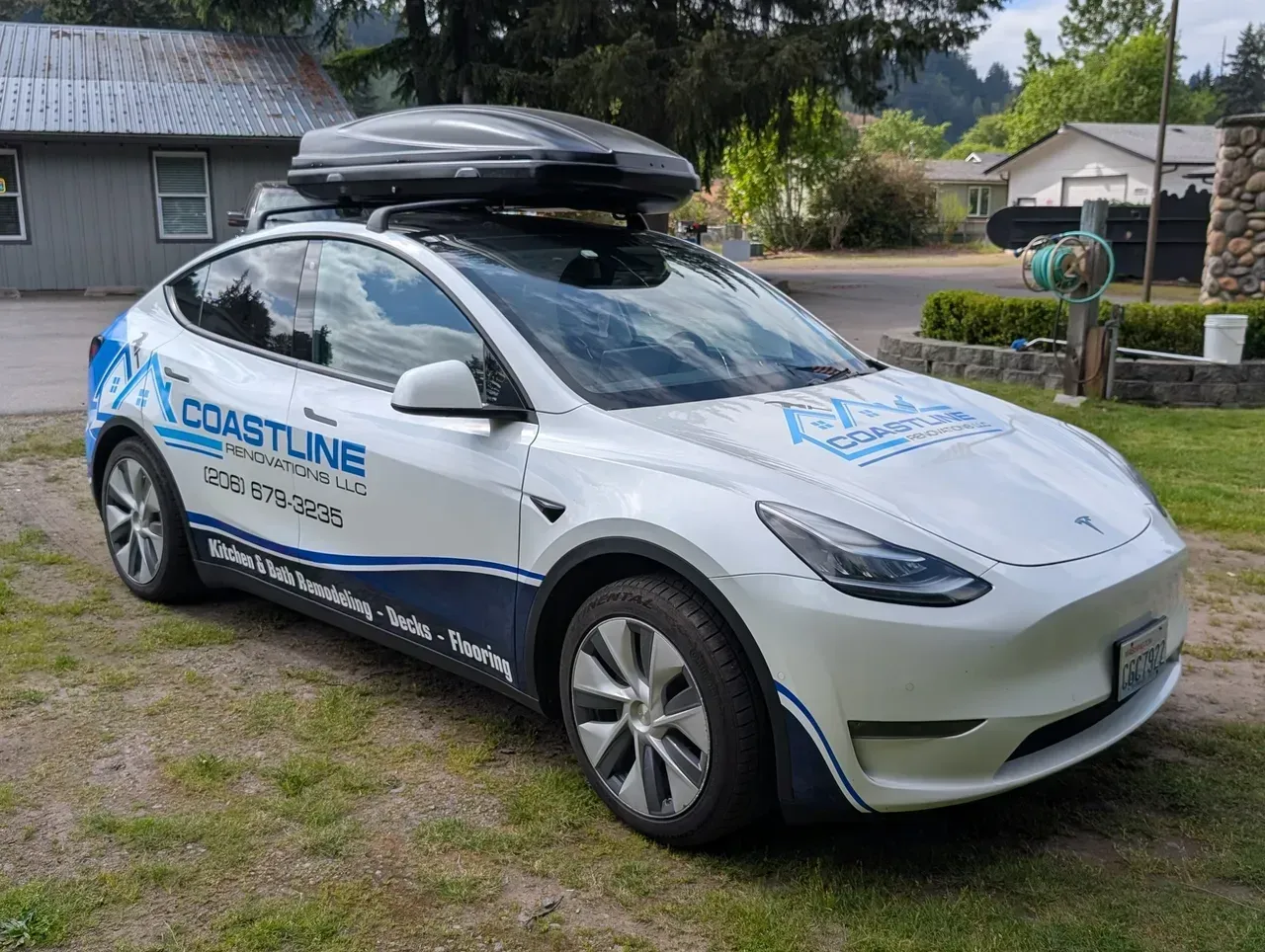 White Coastline-branded Tesla with roof cargo box parked on grass in a residential area