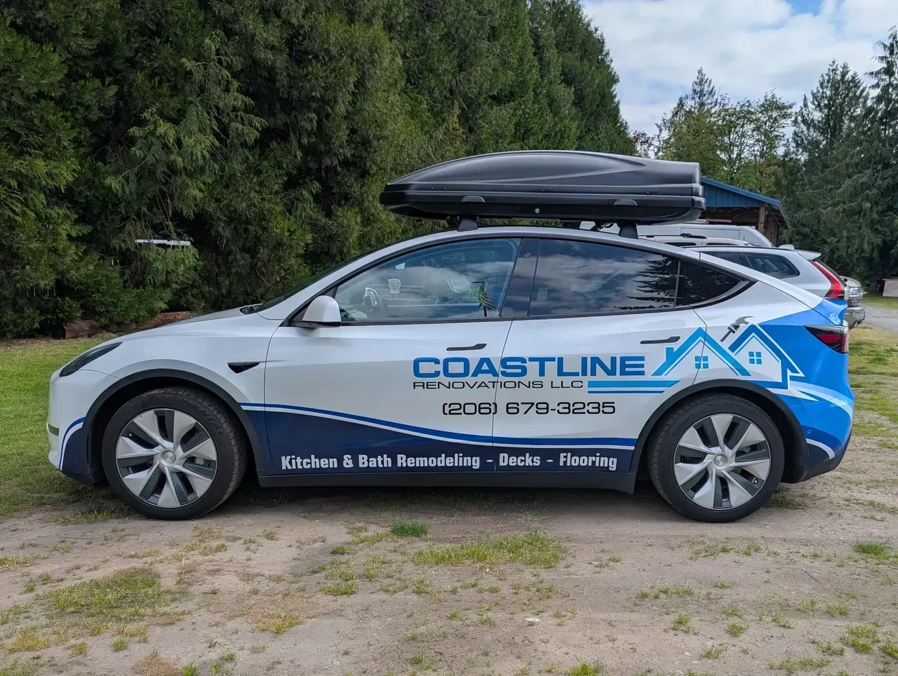 Coastline Driving School car with roof box parked on a gravel lot near trees