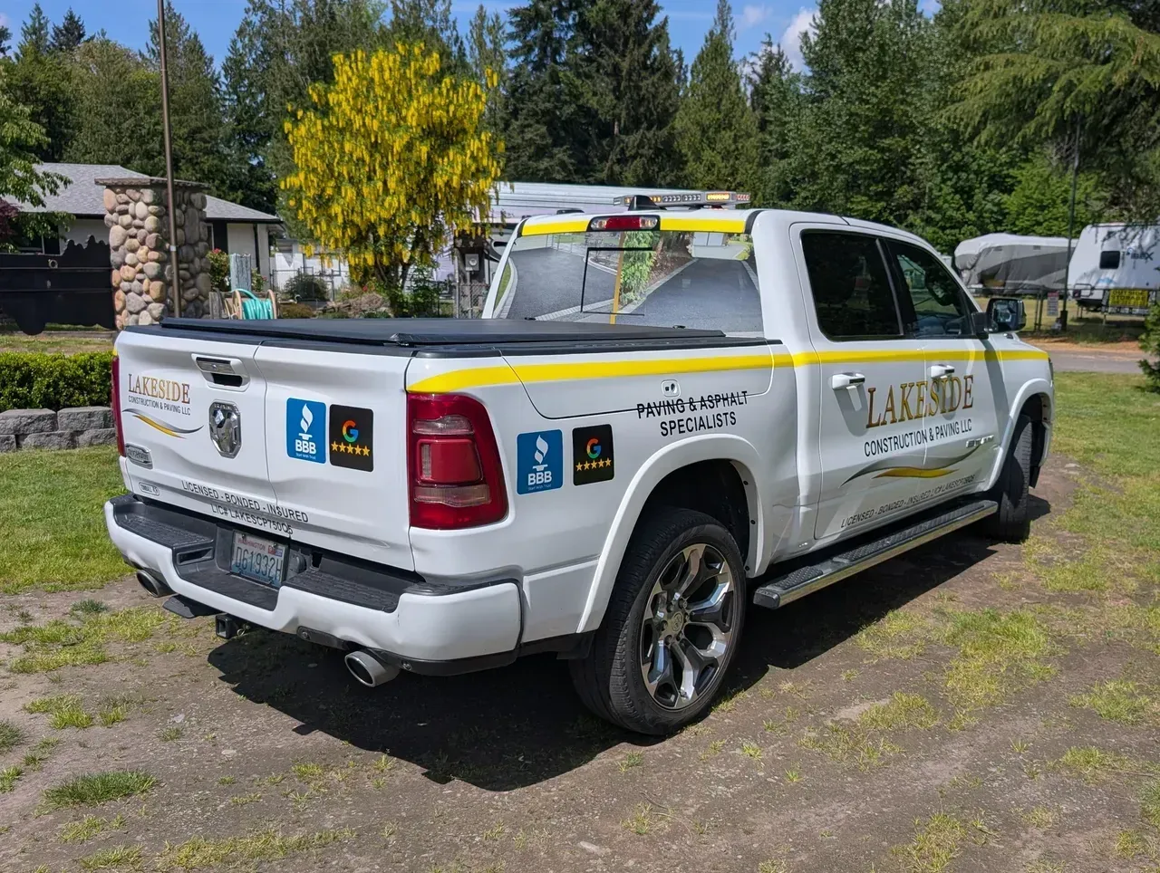White utility pickup truck with decals parked on gravel near trees and houses