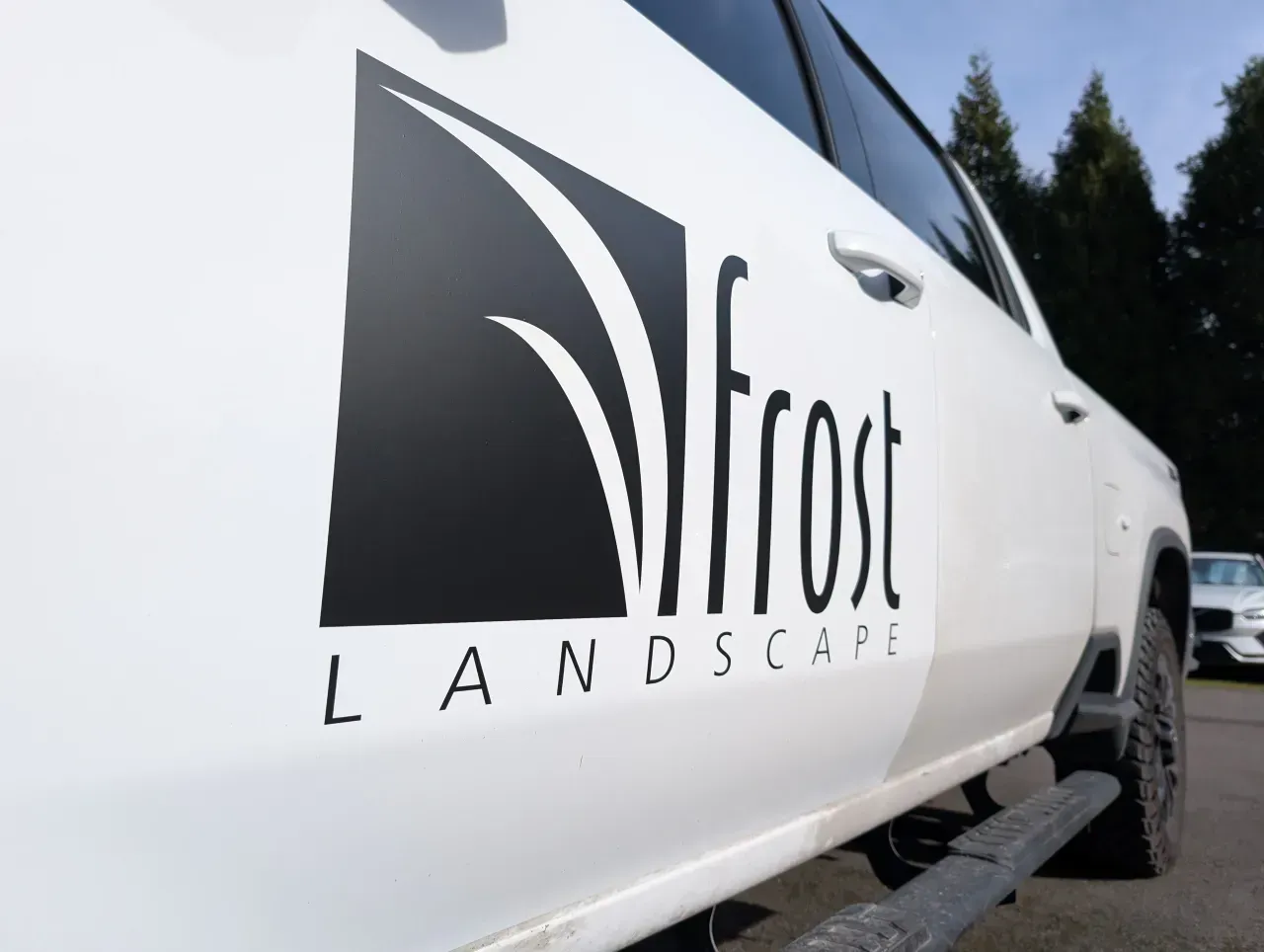 White truck with Frost Landscape logo on the side, parked outdoors by trees and snow