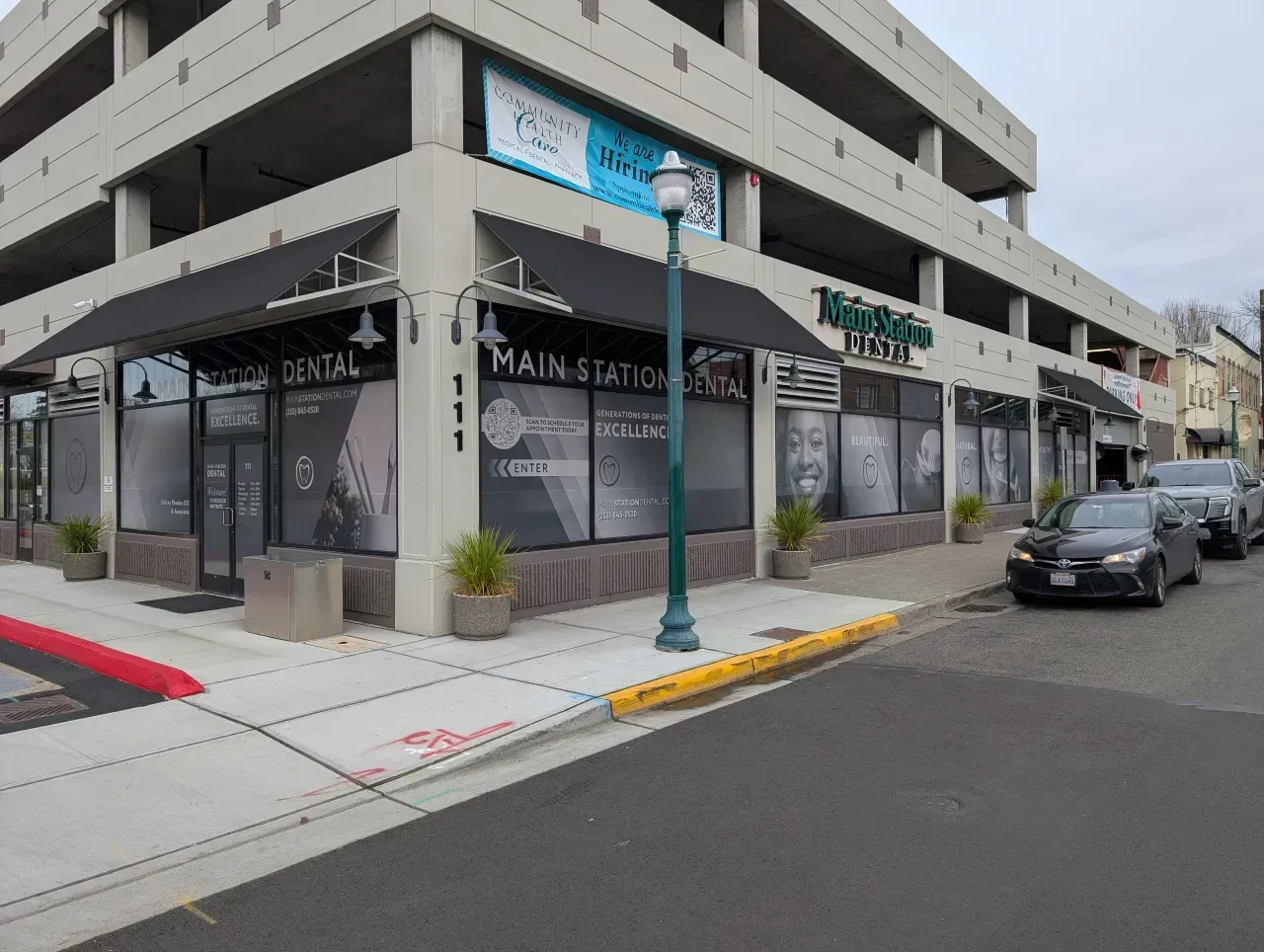 Street corner storefront in a modern building, with parked cars and a storefront sign.