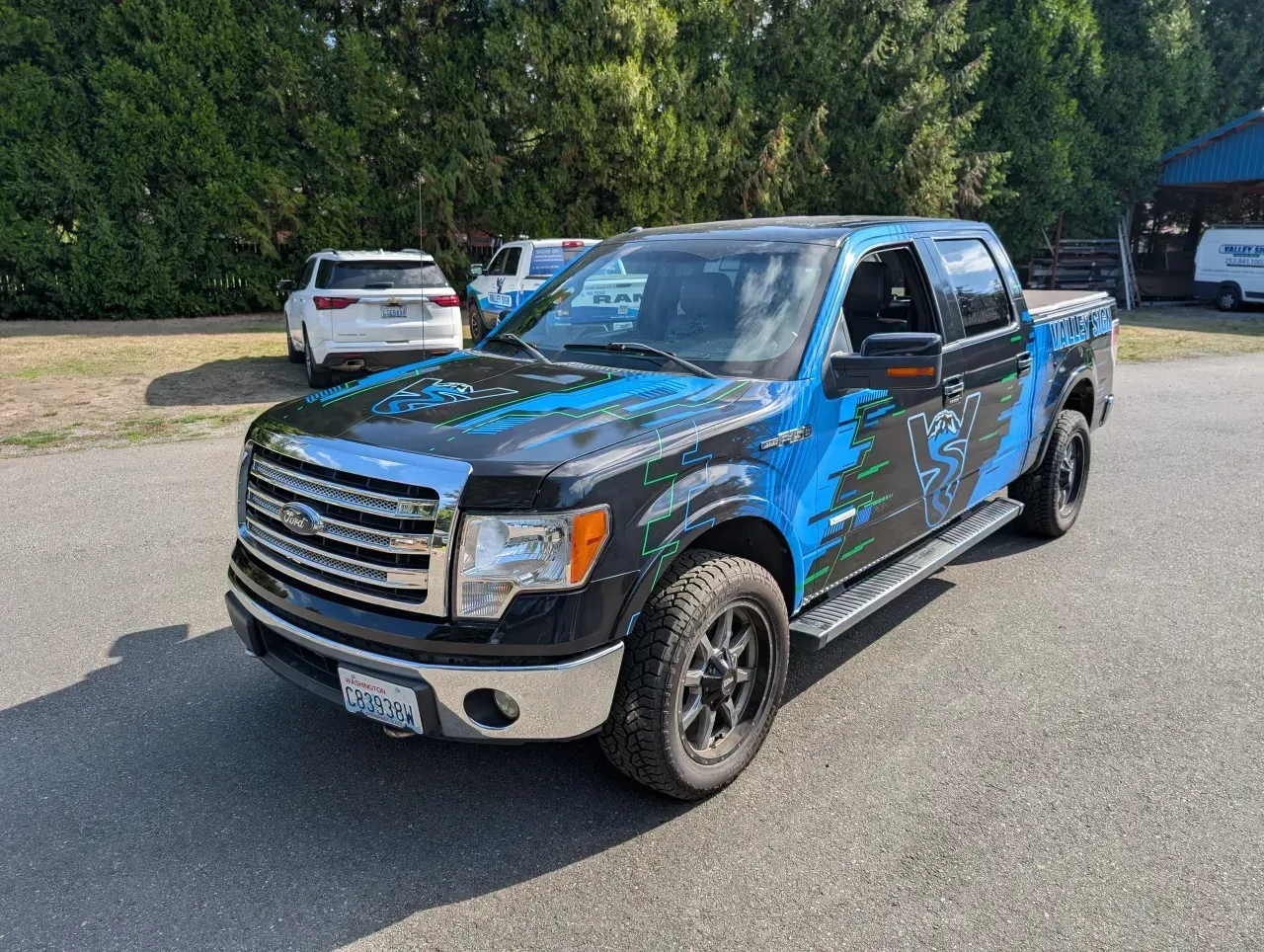 Blue-and-black custom pickup truck parked on a lot, with trees and other cars in the background