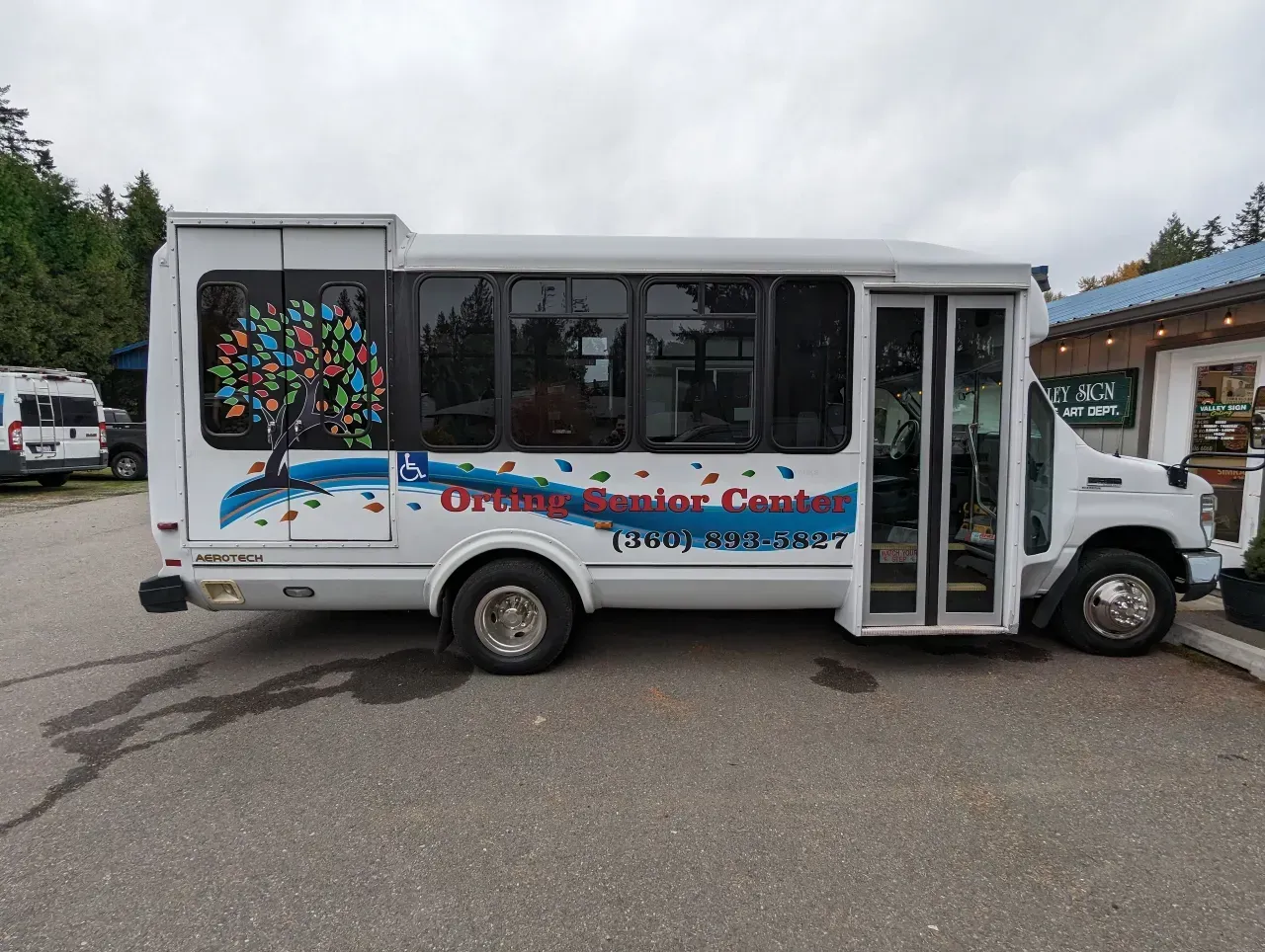 White shuttle bus parked outside a building, with colorful mural graphics and an open passenger door