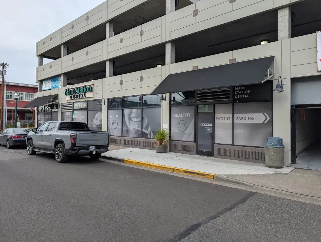 Street view of a storefront strip with a parked silver pickup truck and covered sidewalk parking.