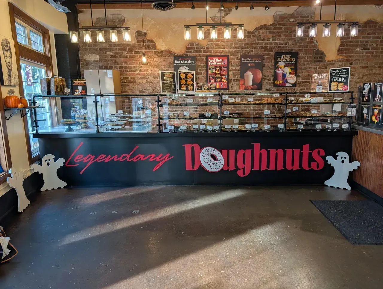 Bakery counter with “Legendary Doughnuts” sign, pastries, brick walls, and hanging lights