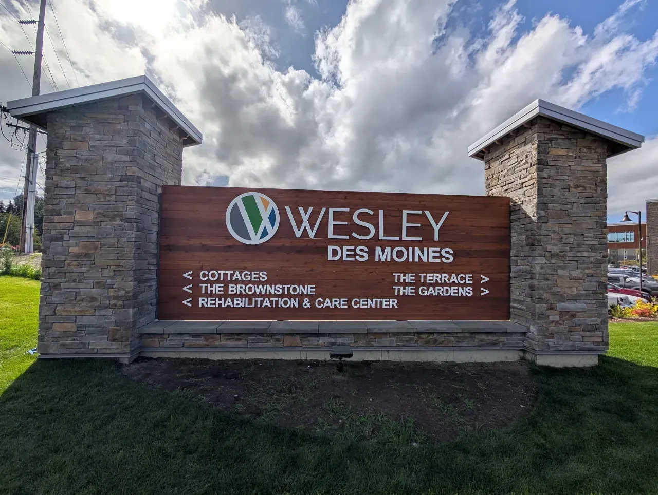 Wesley Des Moines entrance sign with stone pillars, red panel, and landscaping under cloudy sky