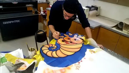 Person decorating a large colorful cake on a worktable in a kitchen.