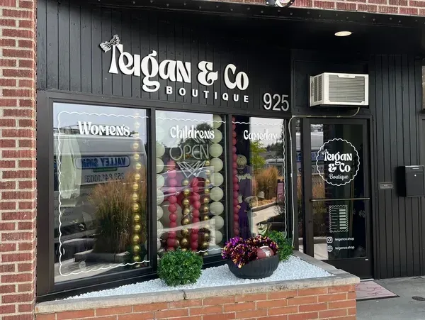 Teigan & Co. boutique storefront with black facade, large windows, and potted flowers by the entrance
