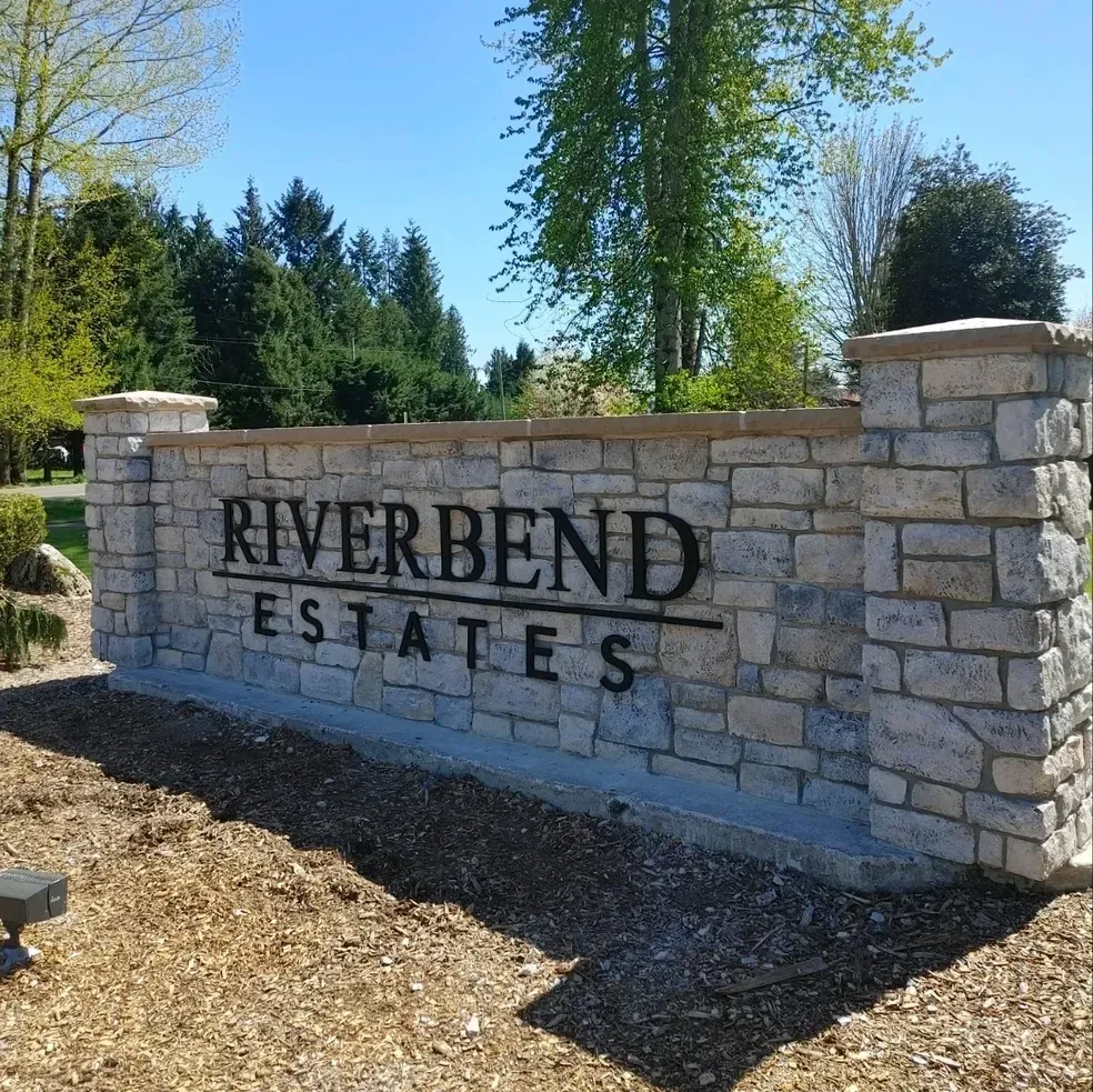 Stone entrance sign reading “RIVERBEND ESTATES” beside trees and blue sky