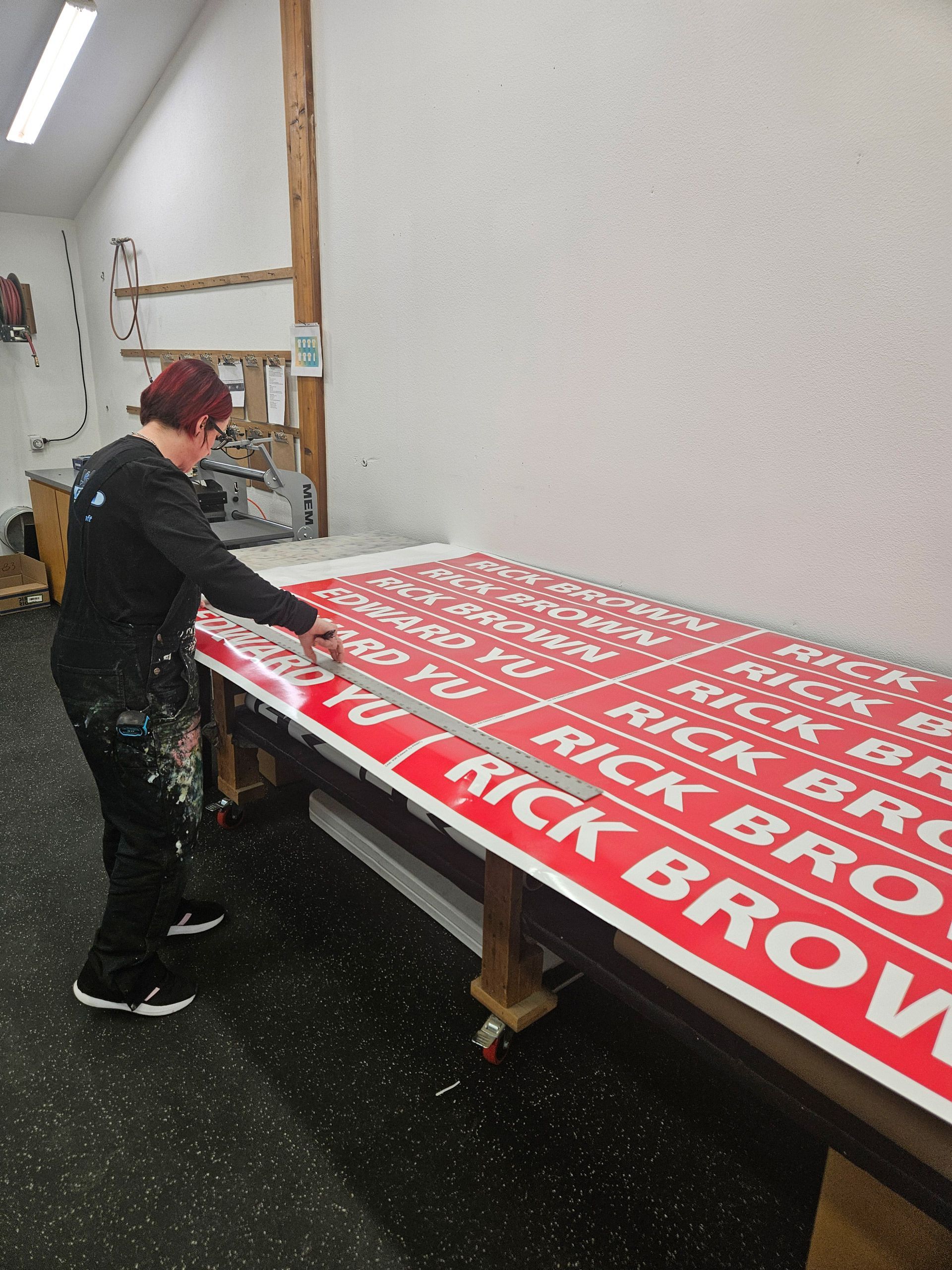 Person applying a large red sign on a worktable in a workshop, with bold white lettering.
