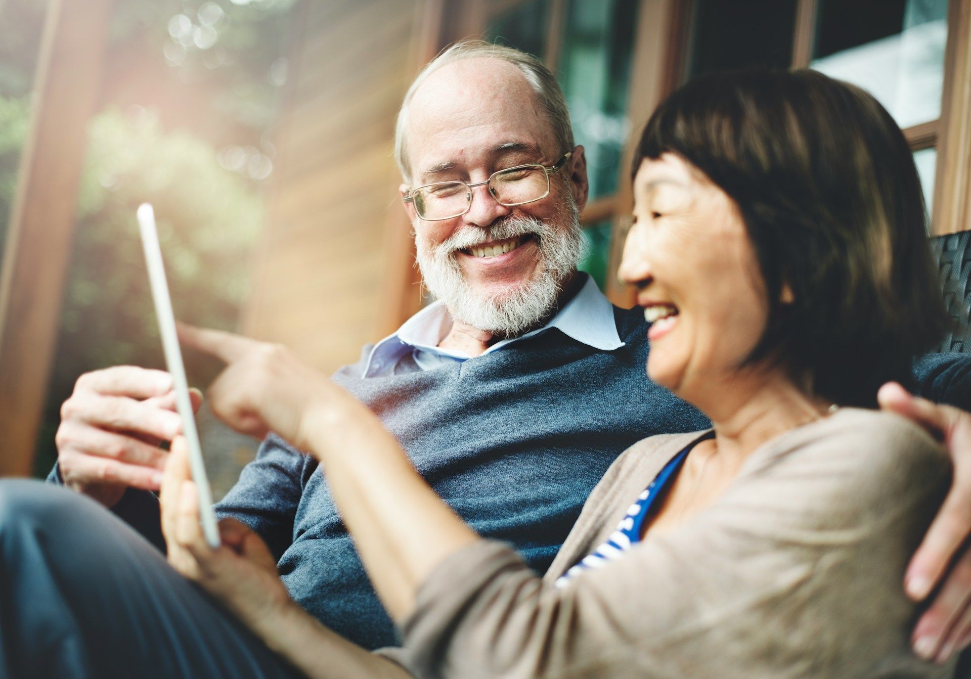 Two people smiling and looking at a tablet in a cozy, sunlit indoor setting