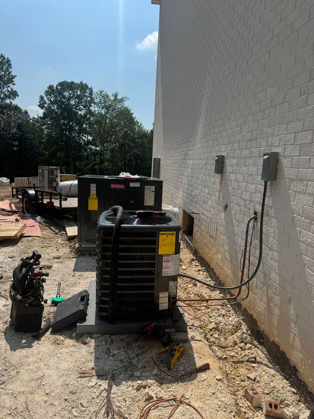 Outdoor HVAC equipment beside a white stucco wall, with hoses and debris on a gravel service area.