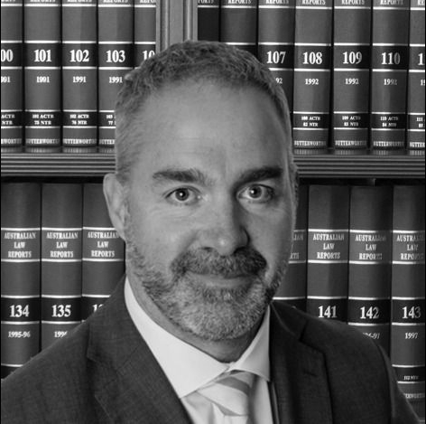 A man in a suit and tie is standing in front of a bookshelf with books on it