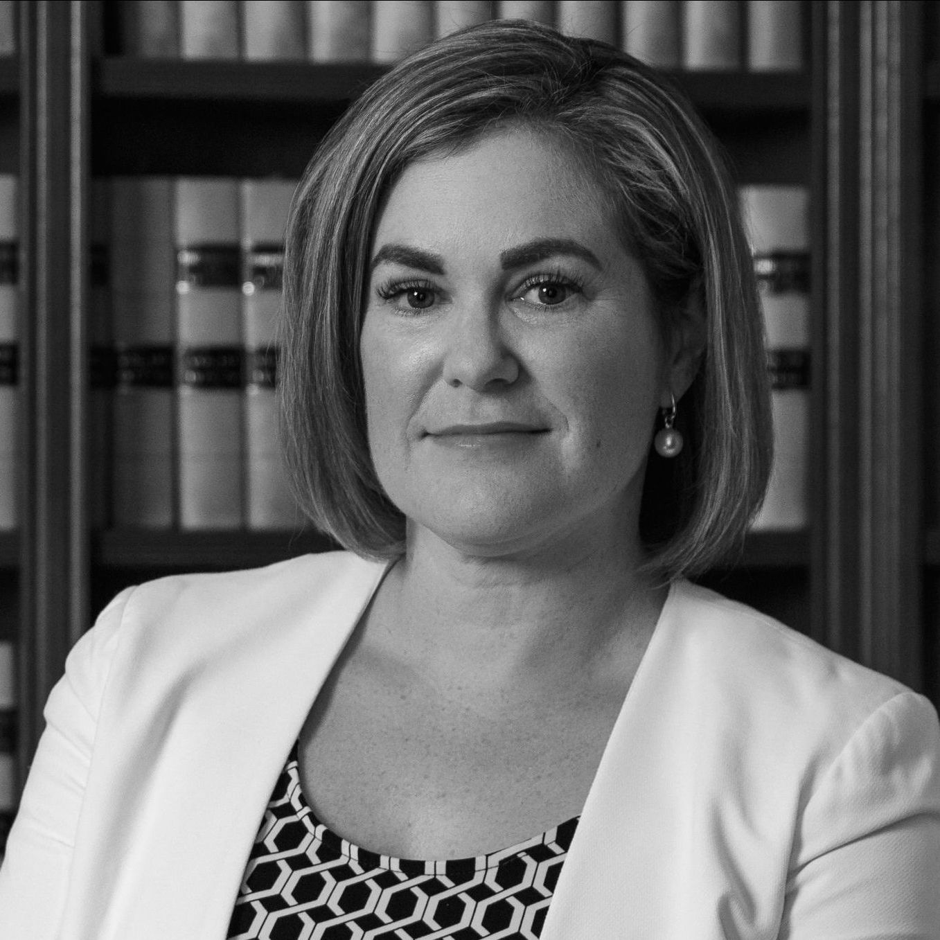 A woman is sitting in front of a bookshelf in a black and white photo.