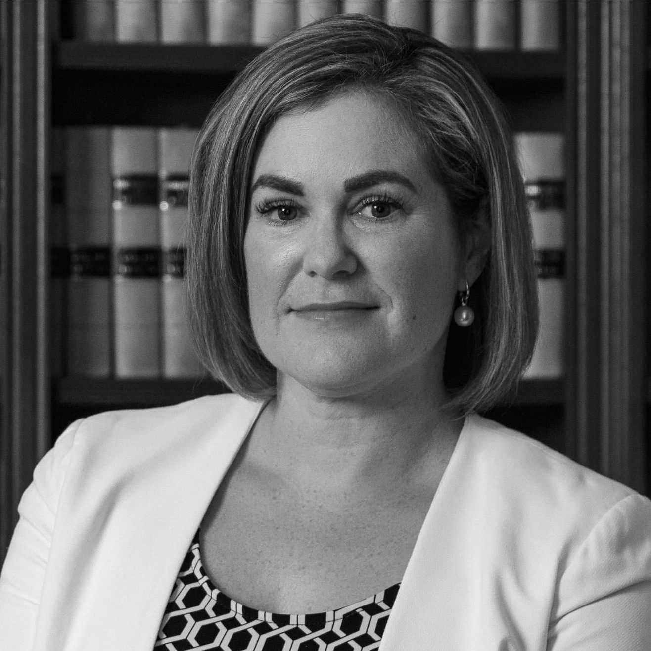 A woman in a white jacket is sitting in front of a bookshelf.