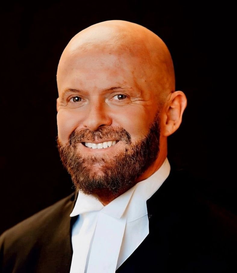 A man wearing glasses and a tuxedo is smiling for the camera.