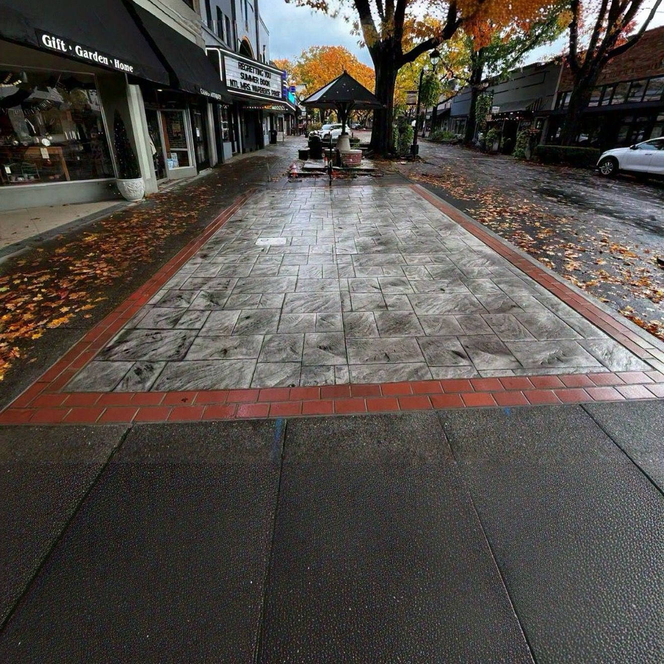 A paved walkway featuring a central stone-tiled rectangular section bordered by red bricks on a town street in autumn.