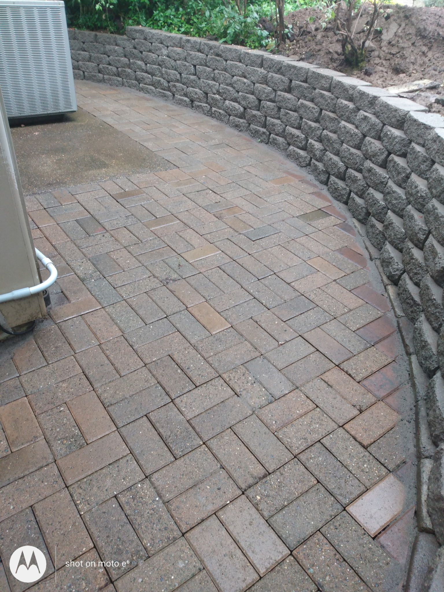 A patio with rectangular reddish-brown pavers laid in a herringbone pattern, bordered by a curved stone retaining wall.