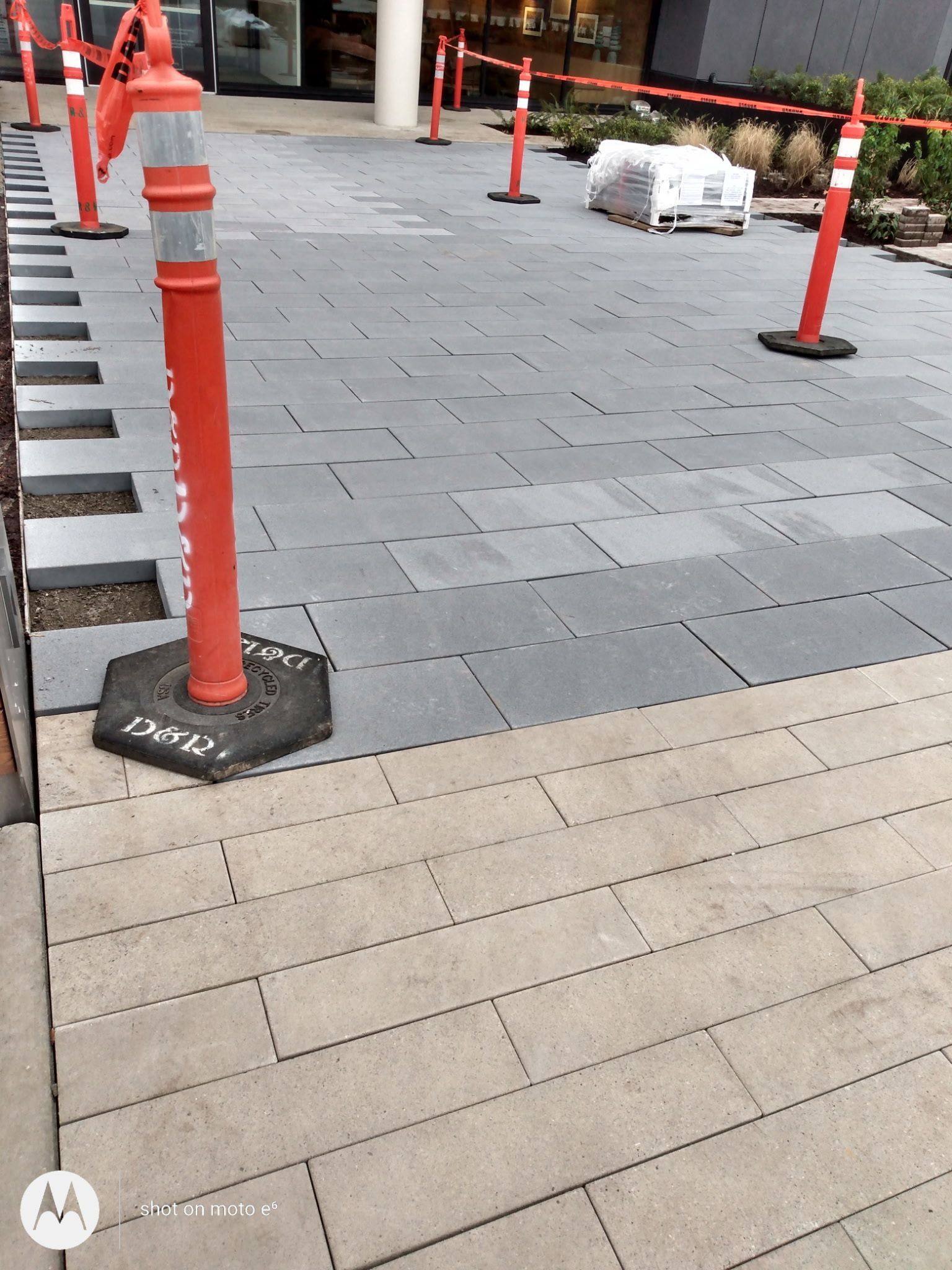 A paved walkway under construction with orange safety cones and tape sectioning off a dark gray section from light pavers.
