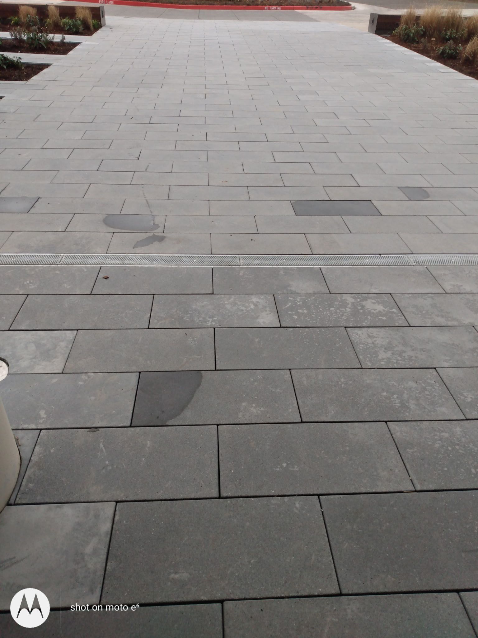 A walkway paved with rectangular gray stone tiles, featuring a horizontal metal drainage grate across the middle.