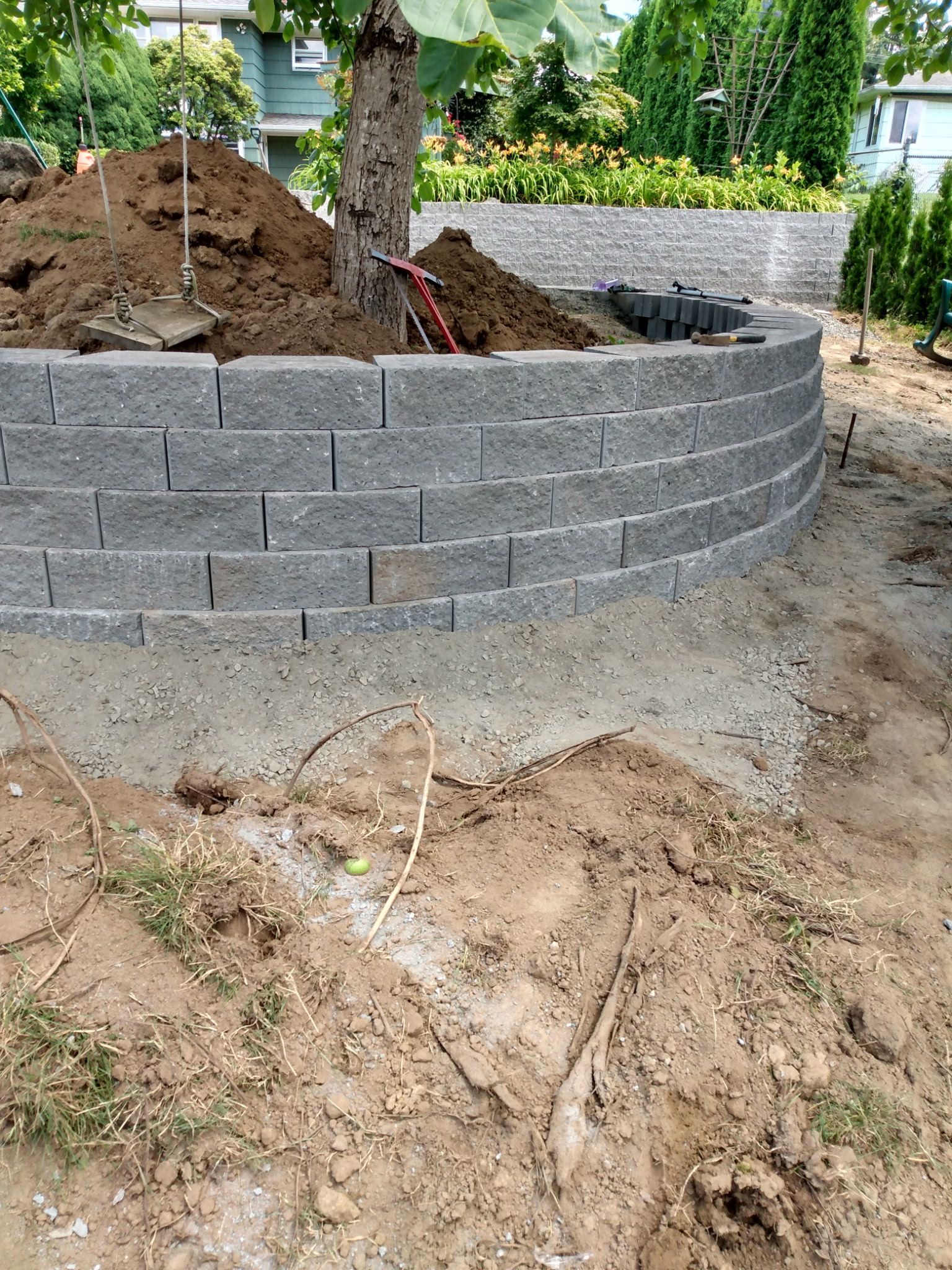 A semi-circular gray stone retaining wall built around a tree in a residential yard.