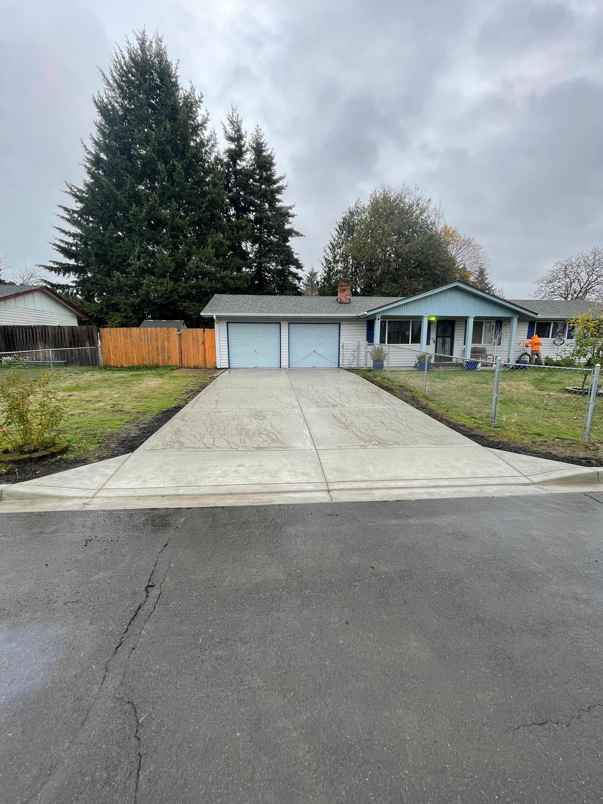 A light blue, single-story house with a two-car garage and a new concrete driveway, set against a cloudy sky.