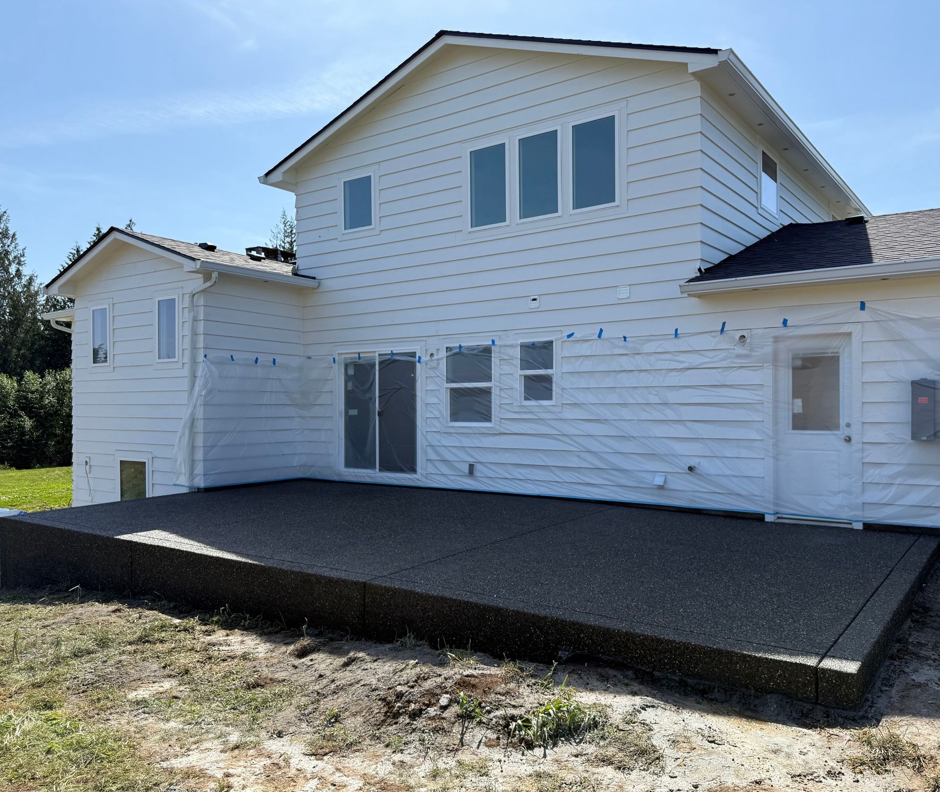 A white two-story house with a newly installed dark, textured concrete patio on a sunny day.