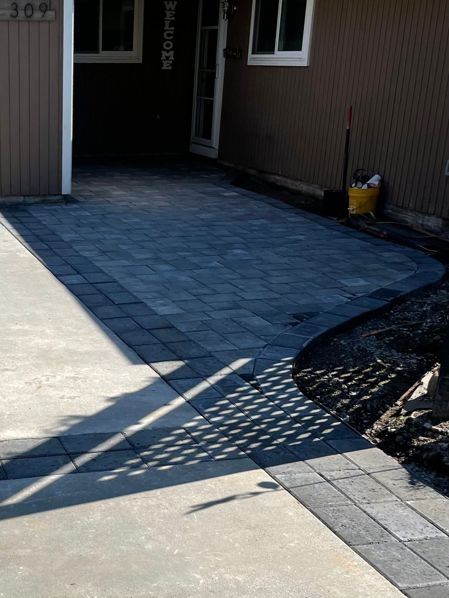 A paved walkway featuring gray rectangular stones with a dark charcoal border leading to a residential front entrance.