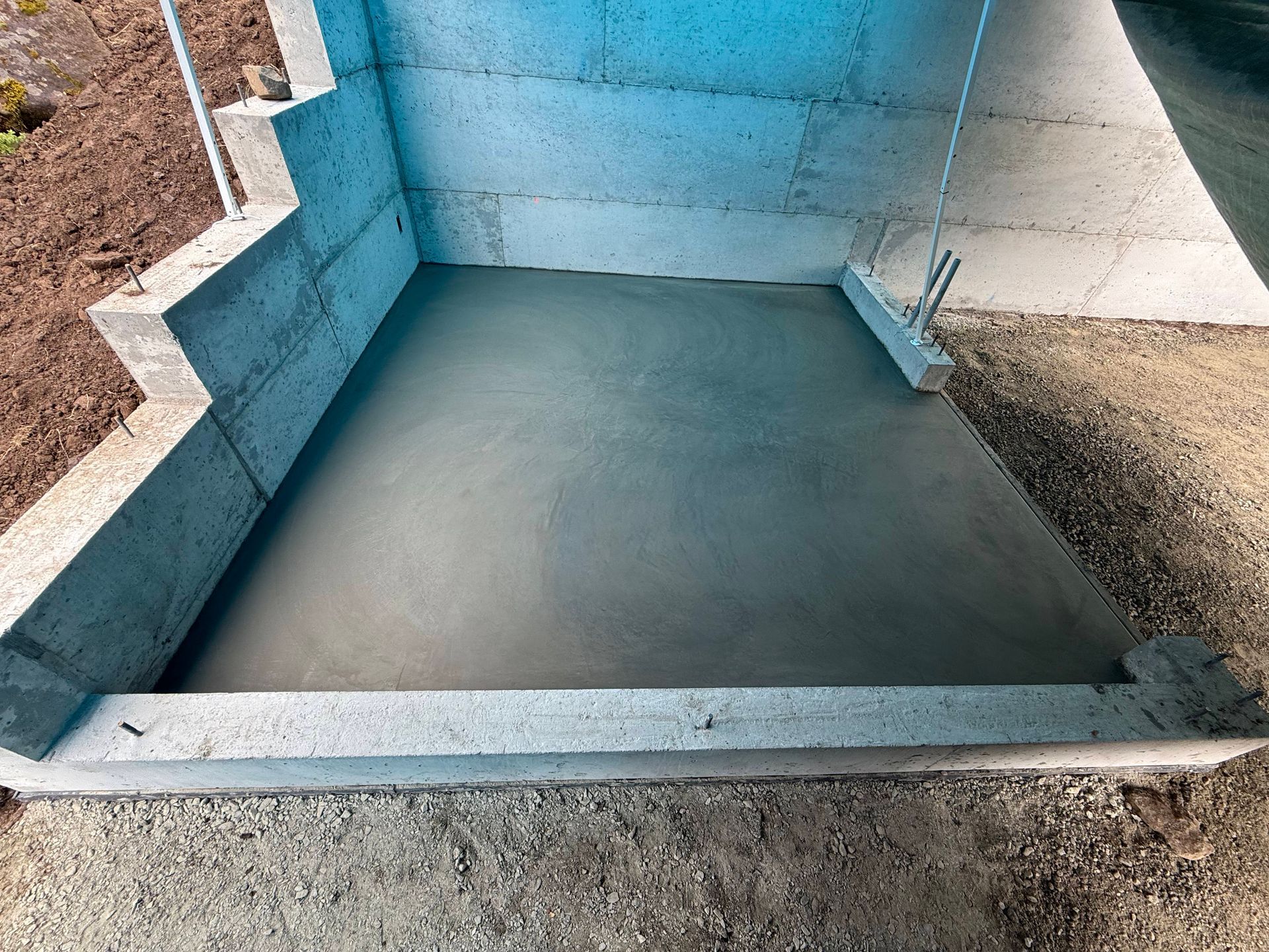 Freshly poured concrete slab set within a light-blue foundation framework outdoors.