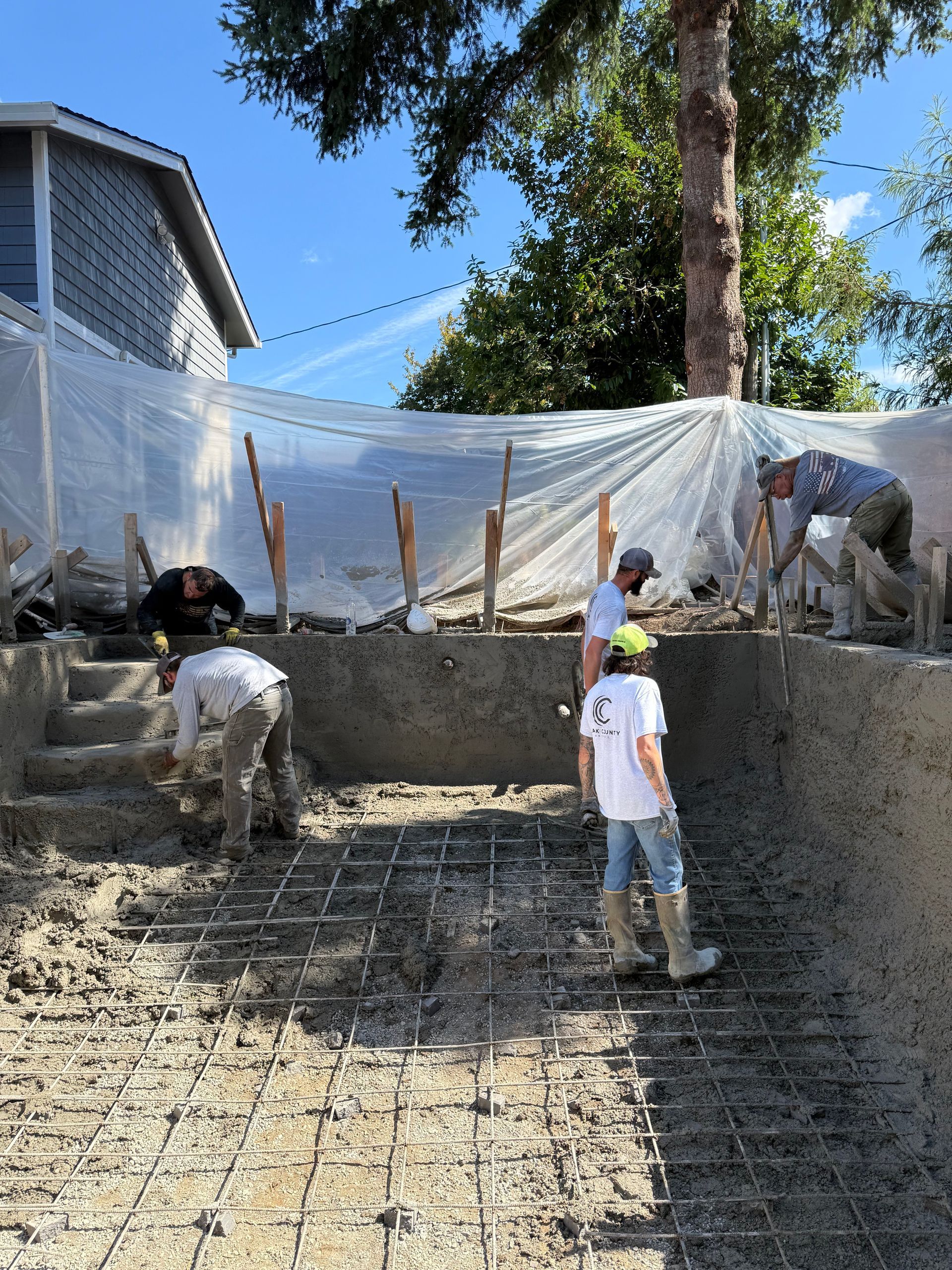 Workers in a construction site laying concrete for a backyard pool in-ground structure.