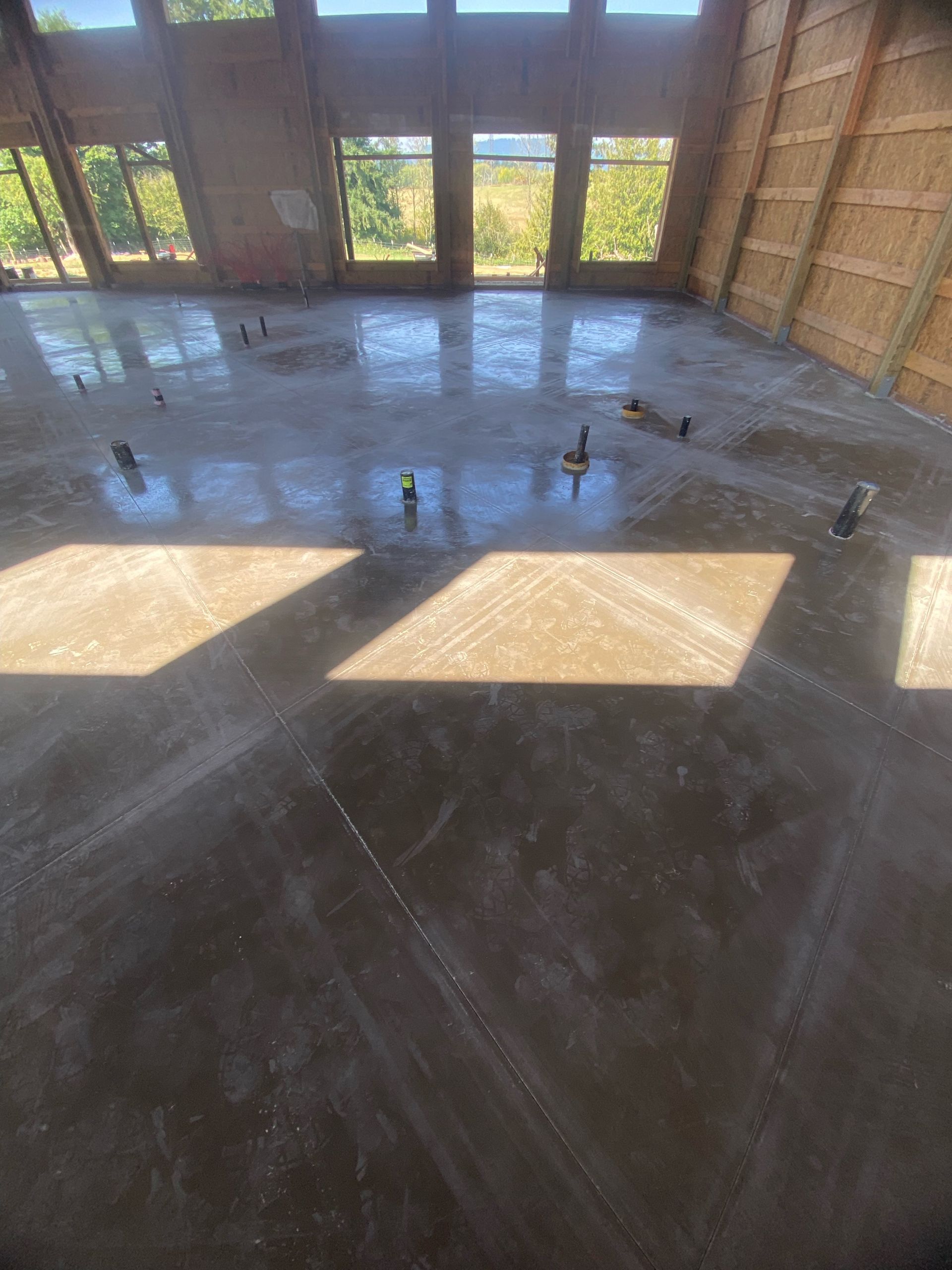 A large interior space with a freshly poured, glossy concrete floor and framing for windows and walls.