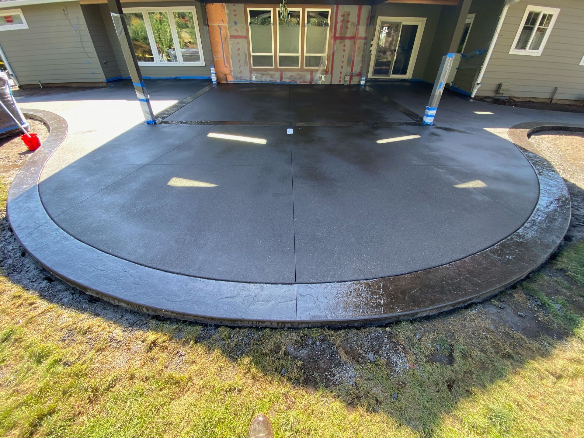 A newly poured, semi-circular gray concrete patio attached to the back of a light-colored house.