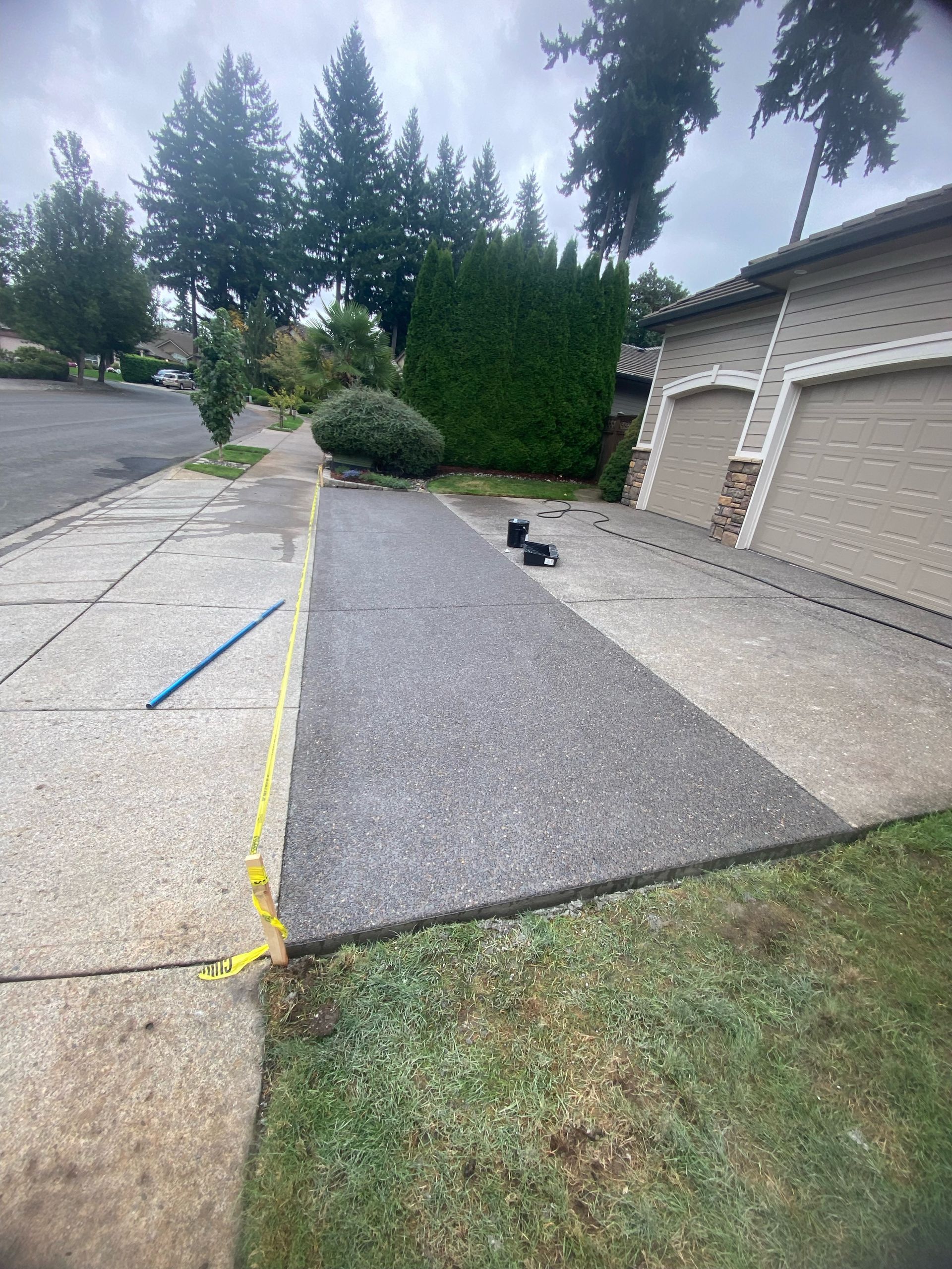 A residential driveway with a freshly paved, dark gray asphalt section next to existing light concrete.