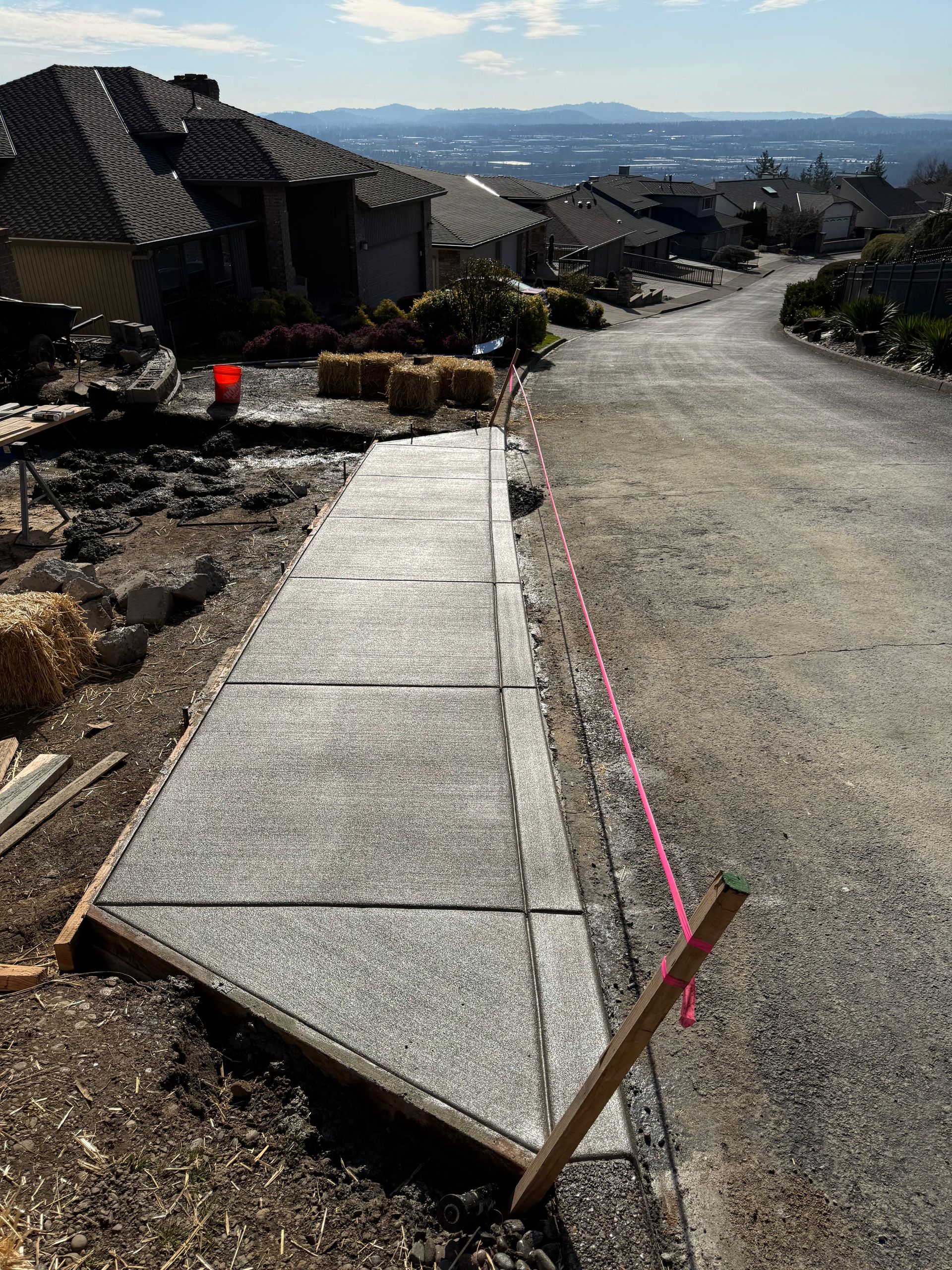 Freshly poured concrete sidewalk sections set alongside a gravel driveway with a residential house in the background.
