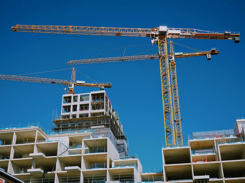 Construction cranes above unfinished buildings under a clear blue sky