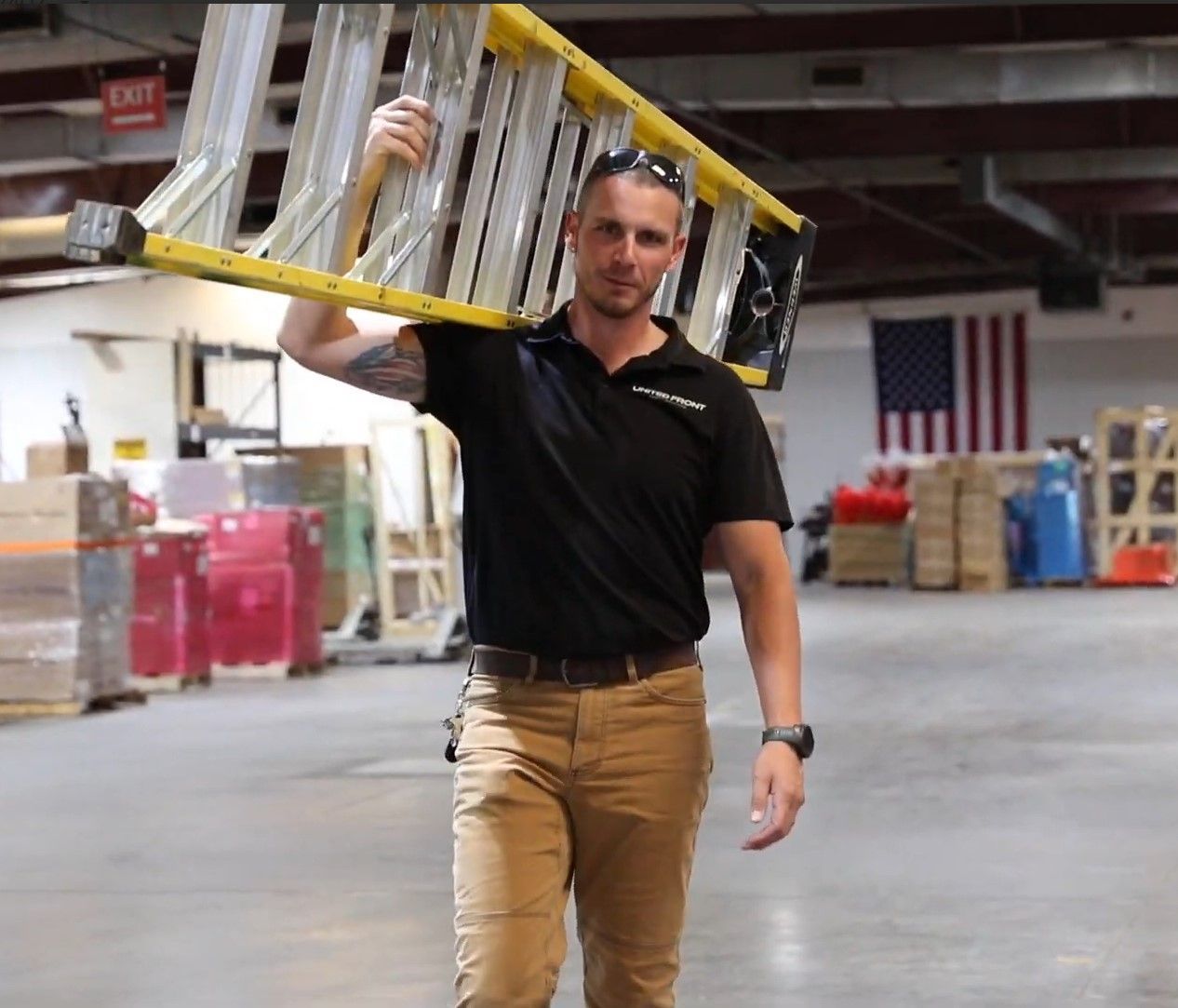 Worker carrying a ladder on his shoulder in a warehouse with an American flag in the background