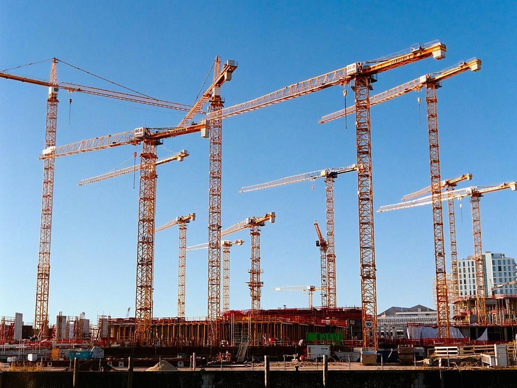 Multiple tower cranes over a building construction site under a clear blue sky