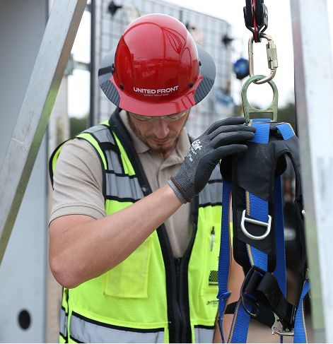 Worker in red hard hat and safety vest inspecting a hanging harness on a construction site
