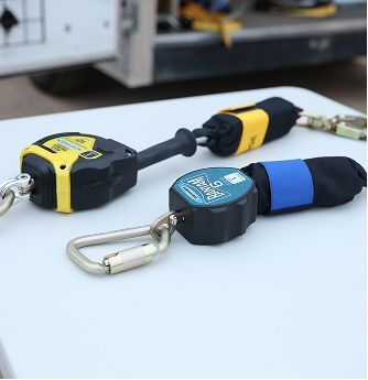 Two retractable safety lanyards with metal clips, black and yellow, on a workbench