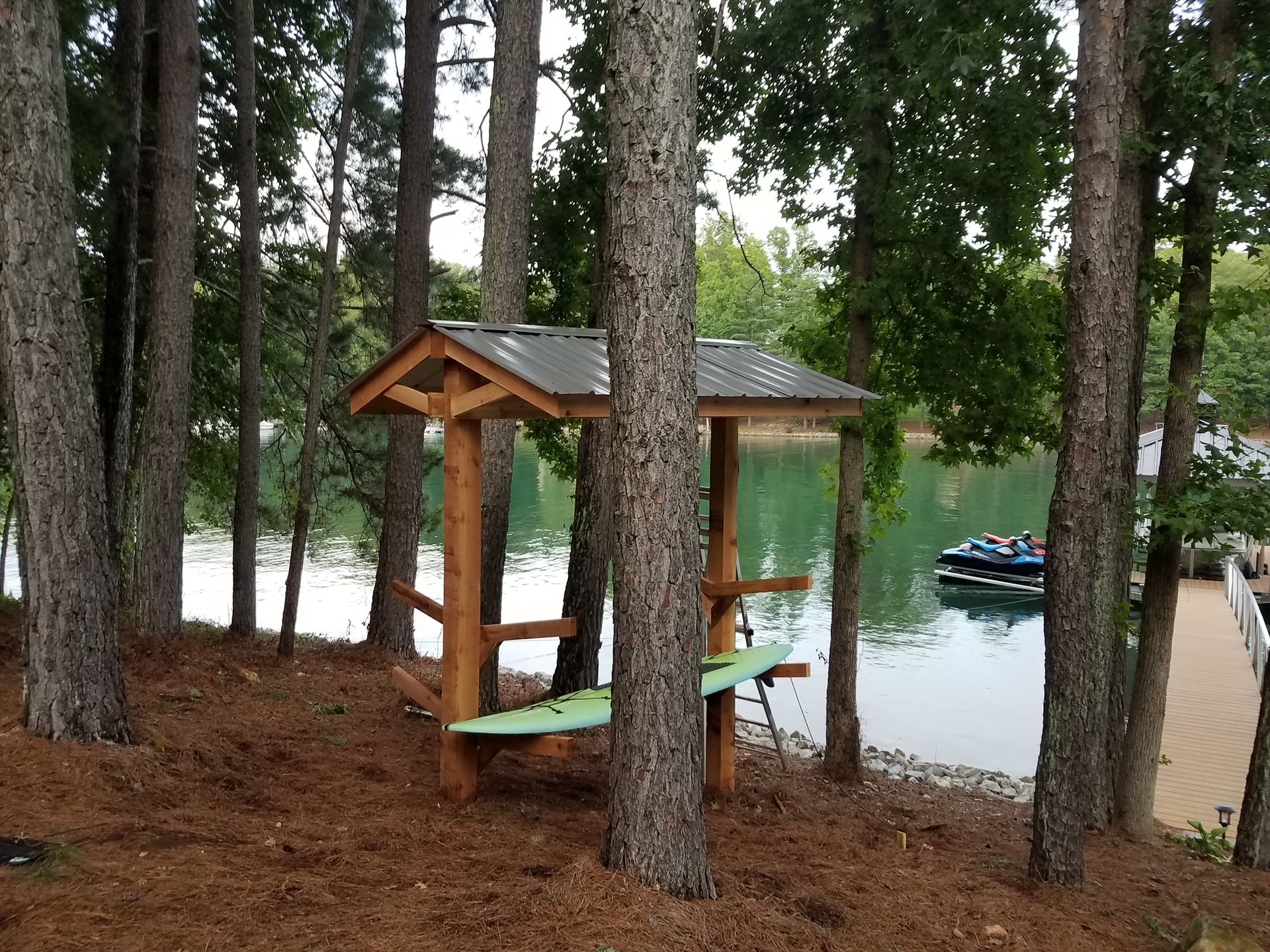A wooden gazebo sits in the middle of a forest near a lake