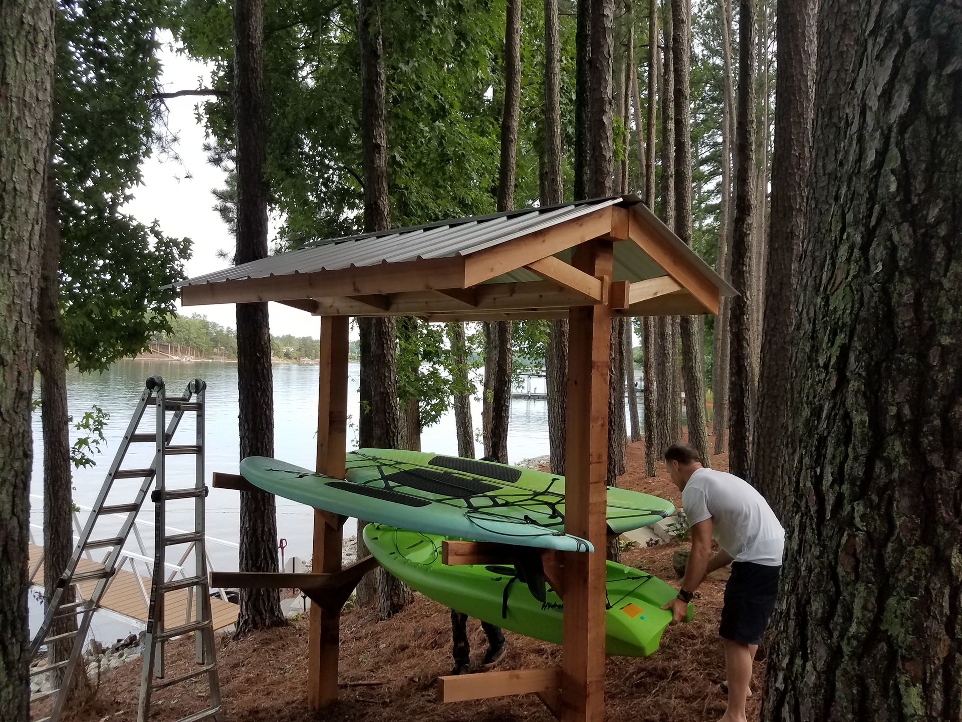 A man is loading kayaks into a wooden rack in the woods