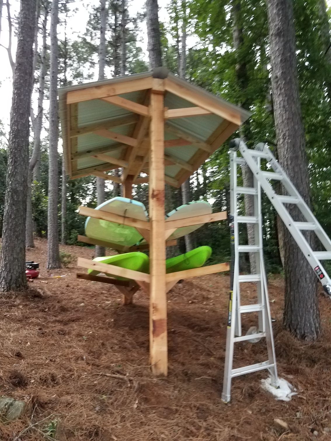 A wooden kayak rack with a ladder attached to it in the woods.
