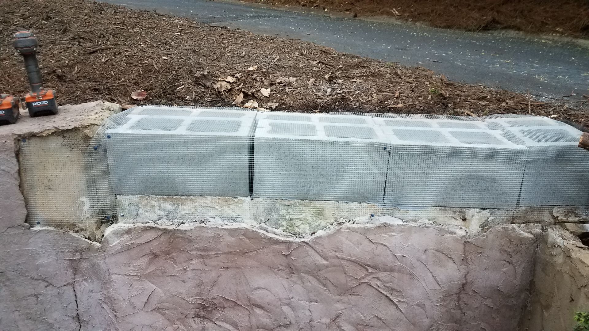 A stack of bricks sitting on top of a concrete surface next to a drill.